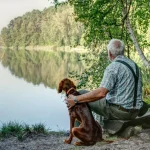 Fig 0.5. Man sitting by lake with dog.